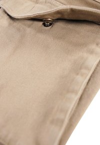 Beige corduroy fabric featuring a folded edge and a metal button with black detail, showcasing a fine ribbed texture.