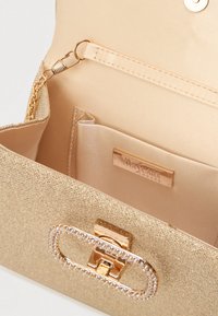 Zlatá kabelka na clutch s textúrovaným povrchom, so zabezpečeným cvokovým uzáverom a vnútorným oddelením s saténovou podšívkou a značkovou platňou.