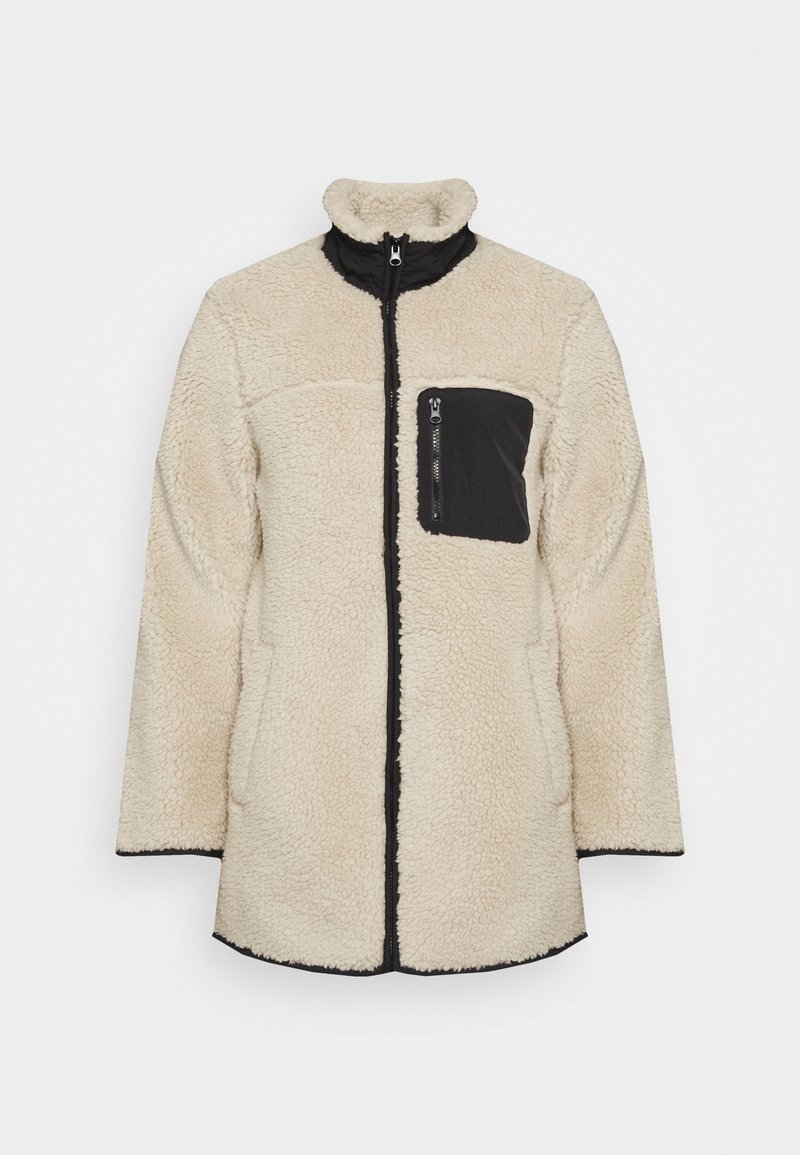 Beige fleecejacka med hög krage, svart dragkedjeförsedd bröstficka och kontrasterande trim. Har ett strukturerat, mjukt material och en lös passform.