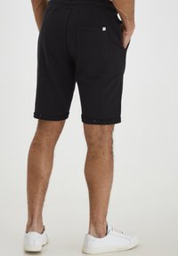 Shorts en coton noir avec une coupe décontractée, taille élastique, ourlet replié et une poche arrière avec une petite étiquette. Associés à des baskets blanches.
