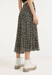 Falda negra con pliegues y un patrón de margaritas, hecha de un material ligero, combinada con botas blancas con cordones y suela gruesa transparente.