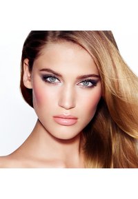 Young woman with smooth skin, green eyes with smoky eye makeup, pink glossy lips, and long flowing blonde hair against a white background.