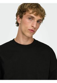 Felpa nera con scollo tondo a costine, tessuto strutturato e vestibilità rilassata. Presenta cuciture delle spalle abbassate e maniche lunghe.