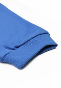 Tissu bleu avec une texture lisse. L'image se concentre sur le poignet, montrant un design côtelé et des coutures soignées le long du bord.