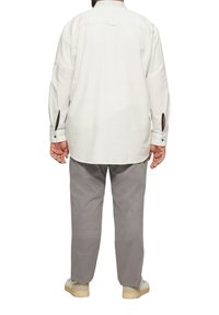 Lange mouwen, lichtbeige shirt met knoopmanchetten en zijsplitten, gecombineerd met losse, grijze broeken en beige schoenen.