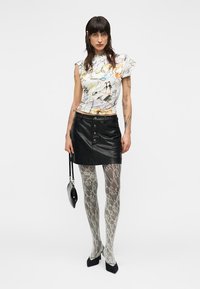 Valkoinen lyhythihainen paita värikkäillä abstrakteilla kuvioilla; musta nahkainen minihame, jossa edessä napit; kuvioidut sukkahousut; musta käsilaukku; mustat korkokengät.