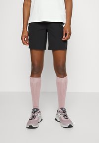 Black athletic shorts with a logo, knee-length pink socks, and gray-pink running shoes with black accents and protective sole.