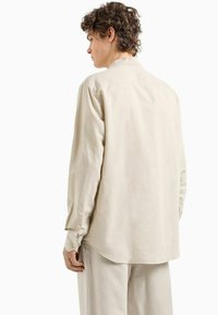Camicia beige a maniche lunghe realizzata in tessuto morbido, con colletto classico e polsini abbottonati, dal taglio rilassato e orlo curvo.