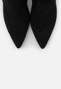 Botines de ante negro de punta afilada con un diseño elegante, que cuentan con una textura suave y detalles de costura a lo largo de los bordes.