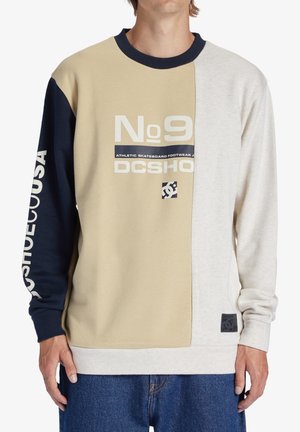 Sudadera con paneles de color beige, marino y gris claro. Presenta logotipos y texto impresos, puños de canalé y un parche cuadrado con el logotipo.