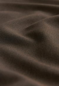 Vue rapprochée et douce d'un tissu marron foncé avec une texture côtelée fine visible et de légers plis créant des ombres et des reflets.