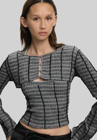 Grå tekstureret top med lodrette sorte striber, vinkelret udskæring og lange ærmer med unikt udsnit foran.