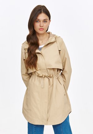 Beżowa kurtka z kapturem, z regulowanym pasem, dwoma bocznymi kieszeniami i zamkiem błyskawicznym z przodu. Wykonana z lekkiego materiału o gładkiej fakturze.