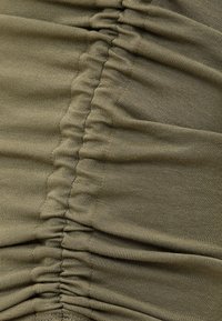 Gros plan d’un tissu extensible vert olive avec des coutures verticales froncées créant des plis texturés.