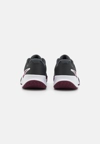 Et par sort og hvid sportsko med maroon-omkransede såler set fra bagsiden på en hvid overflade.
