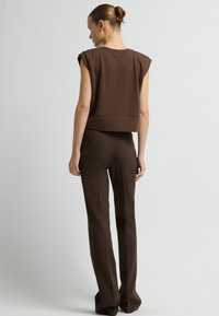 Hnědý crop top se strukturovanými rameny v kombinaci s upravenými hnědými kalhotami. Hladká tkanina, minimalistický design a jemné textury.