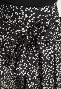 Svart tyg med oregelbundna vita fläckar knytet i en stor rosett vid midjan på ett plagg.