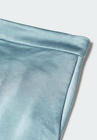 Gros plan d'un tissu satin bleu clair doux avec un bord plié et des coutures visibles sur une surface lisse.