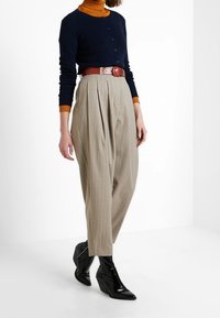 Mörkblå knappad cardigan, orange polotröja, beige byxor med veck och randigt mönster, röd bälte och svarta spetsiga anklar stövlar.