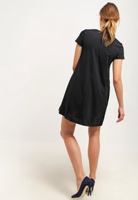 Svart kortärmad klänning med en utsvängd nederkant, tillverkad av mjukt tyg. Bärs med marinblå högklackade skor som framhäver en minimalistisk design.