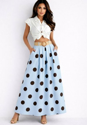 Femme portant un crop top blanc noué et une jupe longue bleu clair avec de grands pois noirs et une ceinture beige avec une boucle ronde.