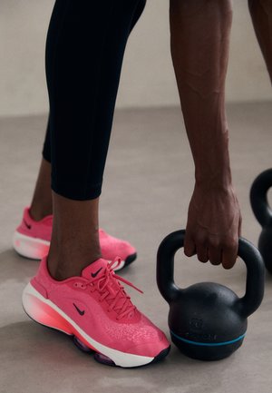 Vaaleanpunaiset Nike-urheilukengät, joissa on tekstuuri, ja valkoinen pohja, sekä musta kettlebell, jossa on sininen yksityiskohta kahvan lähellä.