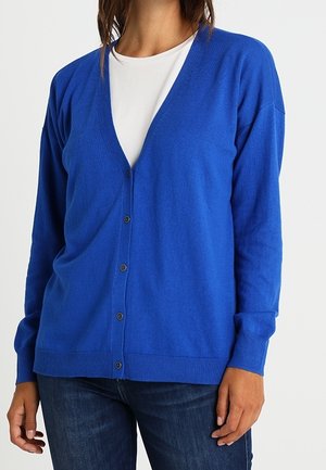 Cardigan bleu en tissu doux, avec un décolleté en V profond, des manches longues et une fermeture à boutons sur le devant. Finitions côtelées au bas et aux poignets.