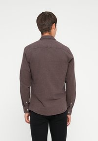 Brun langermet skjorte med teksturert stoff, knappede mansjetter og buet nederkant. Bakview som viser en klassisk krage og en sentral yoke.