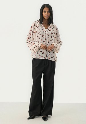White blouse with floral print in red and purple, gathered neckline, and voluminous sleeves, paired with black wide-leg trousers and pointed heels.