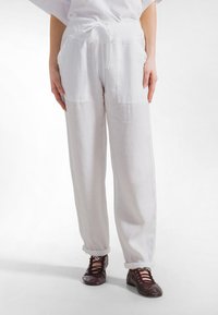 Valkoiset pellavahousut, joissa on kiristysnauha vyötär�öllä, kaksi etutaskua ja käännetyt lahkeet. Yhdistetty ruskeisiin nauhallisiin kenkiin.