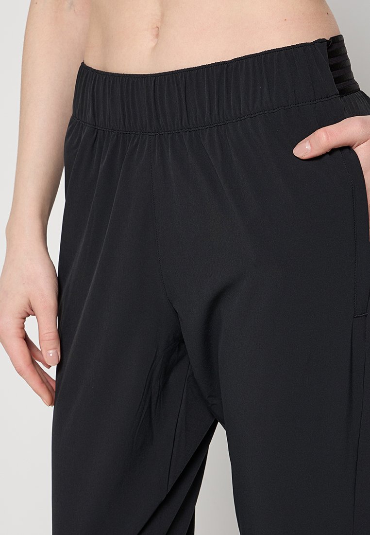 Pantalons noirs à taille élastique en tissu léger et doux. Présente des poches latérales et une coupe décontractée pour le confort. Détails de couture minimaux.