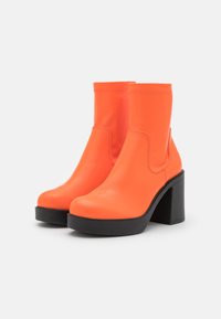 Botas de tobillo naranja neón con un diseño elegante, punta redondeada y alto tacón negro grueso. Hechas de material sintético suave.