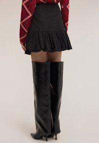 Minifalda negra de cuero sintético con dobladillo fruncido, combinada con botas negras de tacón stiletto hasta el muslo, creando una silueta elegante.