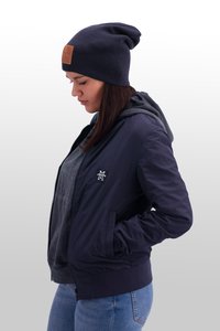 Marineblaues Bomberjacke mit gerippten Bündchen und Taschen, über einem grauen Hoodie getragen. Die Mütze hat ein dunkles Strickmuster und ein braunes Patchdetail.