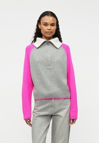 Pull gris avec des manches et un col rose, doté d'un col zippé et d'une texture côtelée. Accents rose vif notables aux poignets et à l'ourlet.