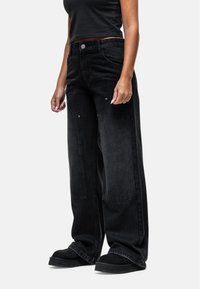 Jeans neri a gamba larga in denim, dotati di tasche frontali e dettagli in metallo. Texture liscia con una finitura leggermente sbiadita.