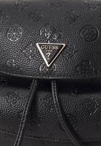 Czarna, teksturowana torebka z wypukłymi wzorami, trójkątną blaszką z logo i uporządkowanym kształtem. Regulowane paski i wyraźne detale.