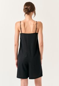 Zwarte mouwloze jumpsuit met verstelbare bandjes, gemaakt van een gladde, lichte stof en met een relaxte pasvorm die tot halverwege de dij reikt.