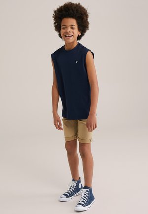 Canotta blu navy, pantaloni corti khaki arrotolati, sneakers alte blu con suola bianca. Design semplice e tessuto morbido; piccolo logo sulla maglietta.