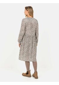 Blomstermønstret, langærmet kjole i lys grå nuancer med et tætsiddende bodice og samlet talje. Parret med brune ankelstøvler.