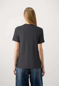 Camiseta negra de algodón con mangas cortas y cuello redondo, presentada en un modelo de espaldas, combinada con jeans de denim azul de corte holgado.