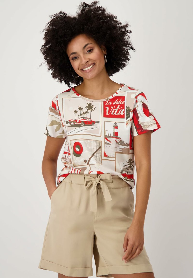 T-shirt manches courtes couleur crème avec un imprimé rétro comprenant des accents rouges, des palmiers, des voitures et des motifs sur le thème du voyage sur un fond clair.