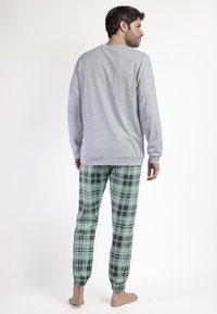 Camisa de manga larga gris combinada con pantalones de pijama de cuadros verdes y negros. Material de algodón suave con puños acanalados en los tobillos.