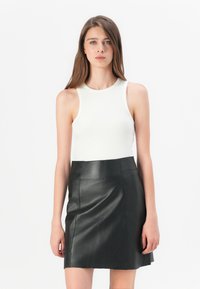 Weißes geripptes Tanktop, kombiniert mit einem schwarzen Leder-Minischrock, der eine glatte Textur und eine figurbetonte Silhouette aufweist.