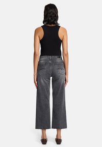 Schwarzes ärmelloses Tanktop, graue weite Jeans mit fransigen Säumen und braune Slipper. Das Outfit hat eine entspannte Passform und minimale Details.