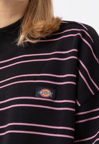 Suéter negro con rayas horizontales rosas, textura de punto, cuello acanalado y un pequeño parche rectangular con el logo de Dickies en el frente.