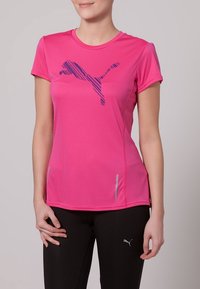 Camiseta atlética rosa de Puma con mangas cortas, que presenta un logo de rayas azules en el pecho y dos sutiles bolsillos laterales. Textura suave.