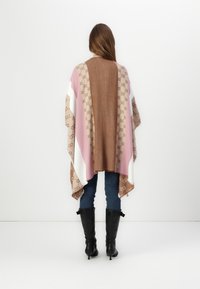 Brun og lyserød mønstret indpakning med hvide og brune striber. Blødt materiale, løs design, båret over blå jeans og sorte knæhøje støvler.