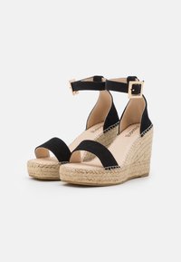 Black suede wedge sandals with an open toe, ankle strap featuring a square buckle, and a woven straw midsole.