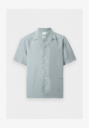 Jasnoniebieska koszula na krótki rękaw z kołnierzykiem, zapinana na pięć białych guzików z przodu, z subtelnym logo Calvin Klein przy dolnym brzegu.